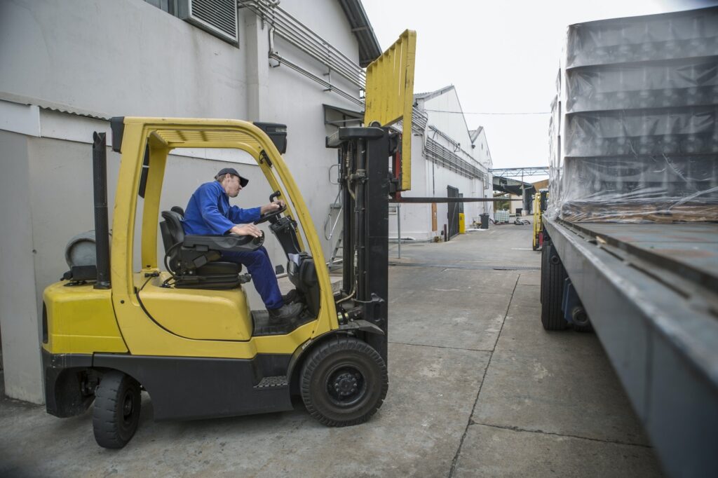 Forklift driver loading pallet onto truck at packaging factory