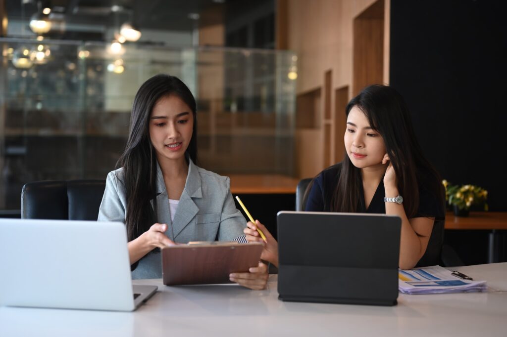 Two businesswoman consulting data on digital tablet while sitting together in modern office.